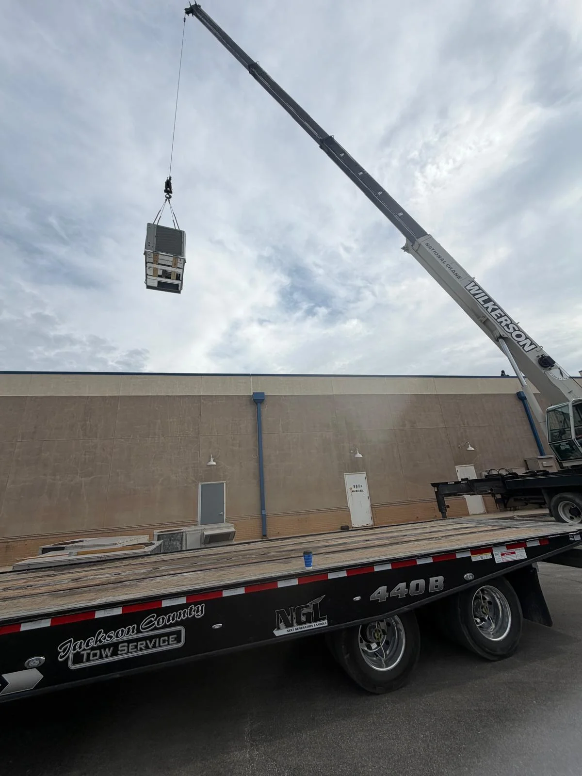Crane lifting commercial rooftop HVAC package unit from transport flatbed